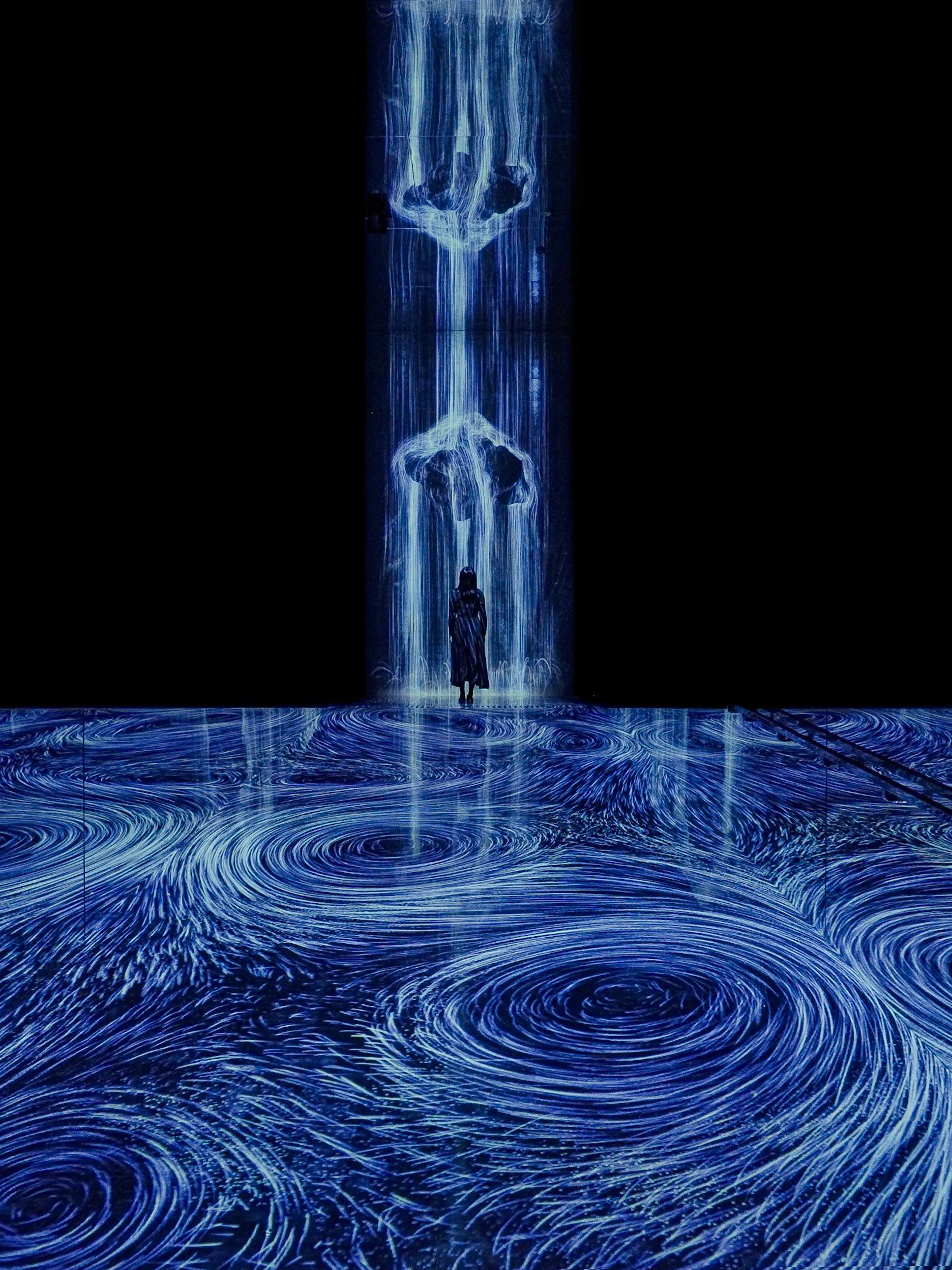 Interactive digital art installation with swirling blue vortices and a person standing in the flow.