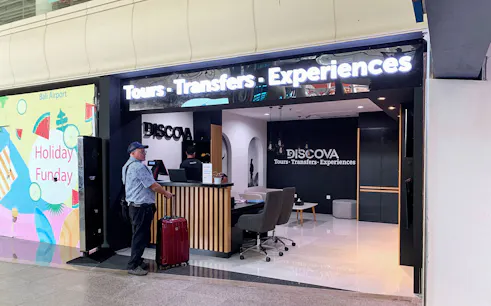 Man with suitcase at Discova Tours counter, Bali Airport.