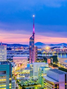Fukuoka Tower illuminated at dusk with cityscape and coastline in Fukuoka, Japan.