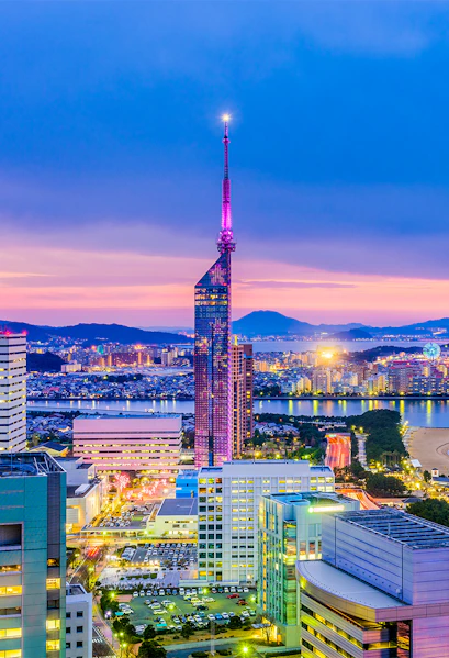 Fukuoka Tower illuminated at dusk with cityscape and coastline in Fukuoka, Japan.