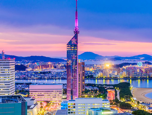 Fukuoka Tower illuminated at dusk with cityscape and coastline in Fukuoka, Japan.