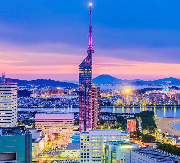 Fukuoka Tower illuminated at dusk with cityscape and coastline in Fukuoka, Japan.