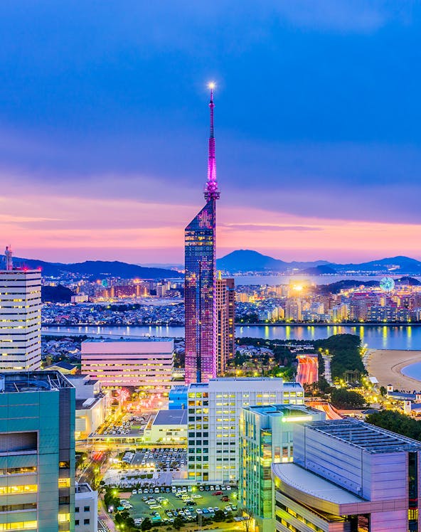 Fukuoka Tower illuminated at dusk with cityscape and coastline in Fukuoka, Japan.