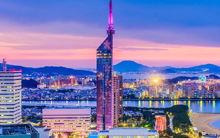 Fukuoka Tower illuminated at dusk with cityscape and coastline in Fukuoka, Japan.