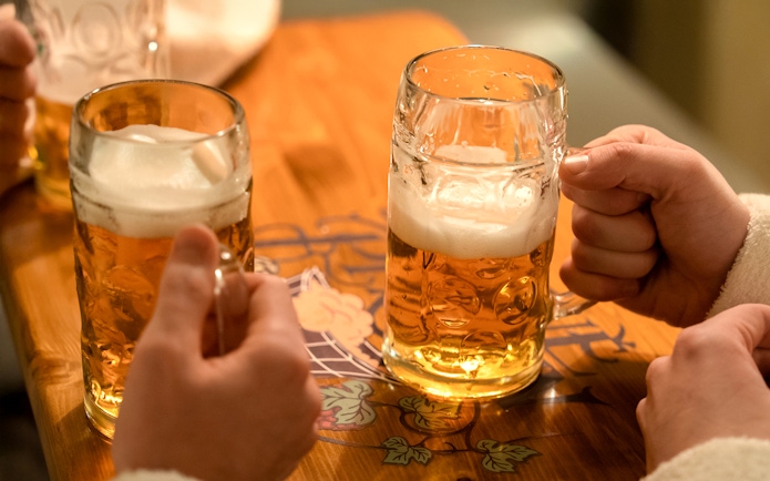 Hands holding beer mugs on a wooden table.