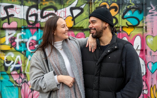 Couple smiling in front of colorful graffiti at NDSM, Amsterdam.