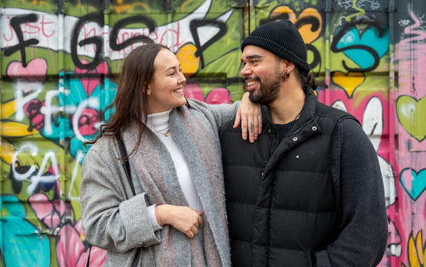 Couple smiling in front of colorful graffiti at NDSM, Amsterdam.