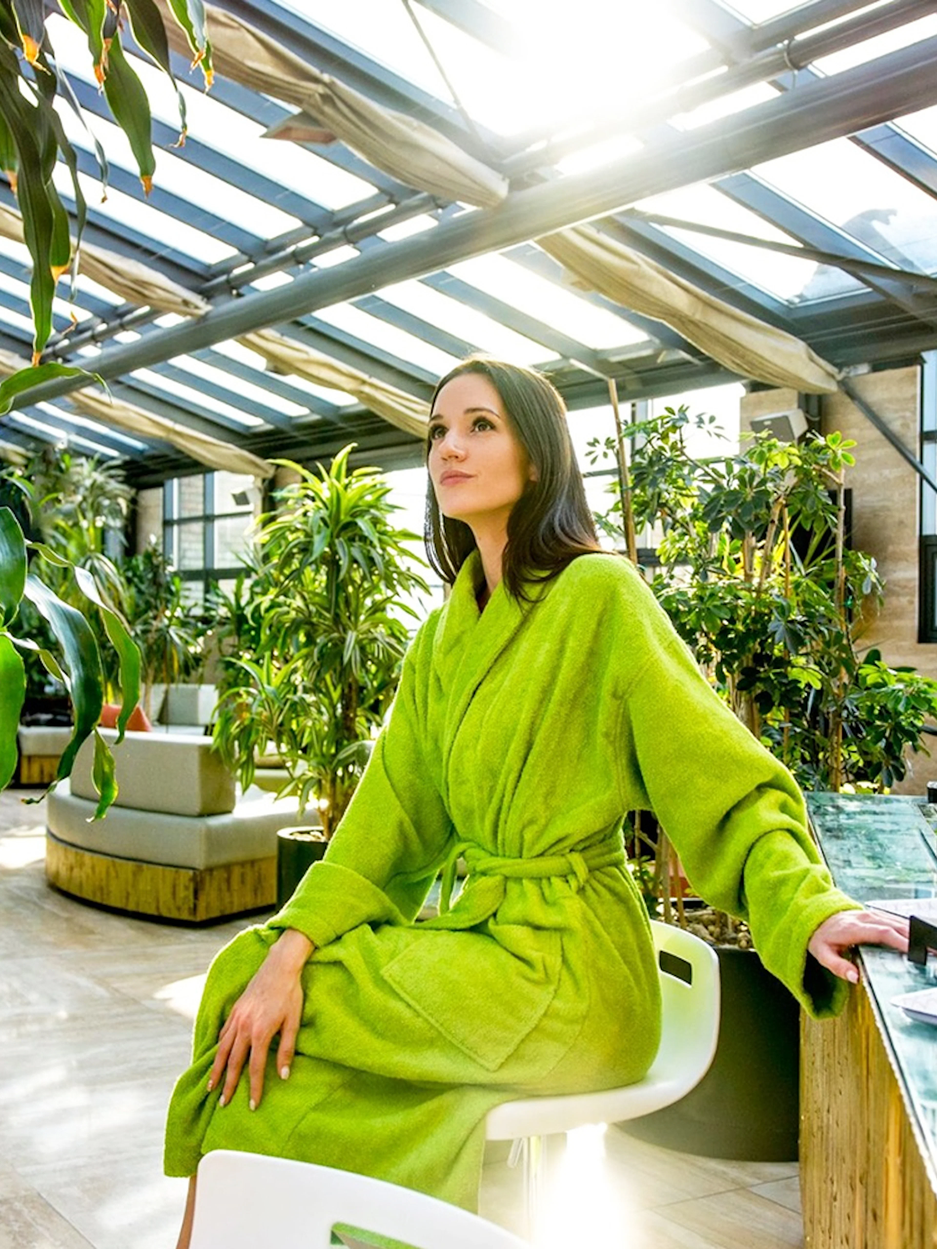 Person in green robe relaxing at Szechenyi Bath spa with plants and refreshments nearby.