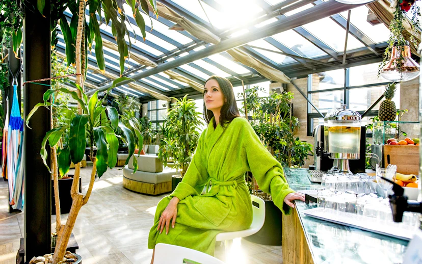 Person in green robe relaxing at Szechenyi Bath spa with plants and refreshments nearby.