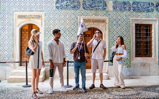 Tour group with guide at Topkapi Palace Museum, Istanbul, near ornate tiled wall.