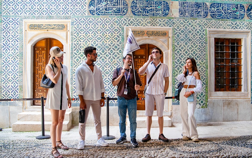 Tour group with guide at Topkapi Palace Museum, Istanbul, near ornate tiled wall.