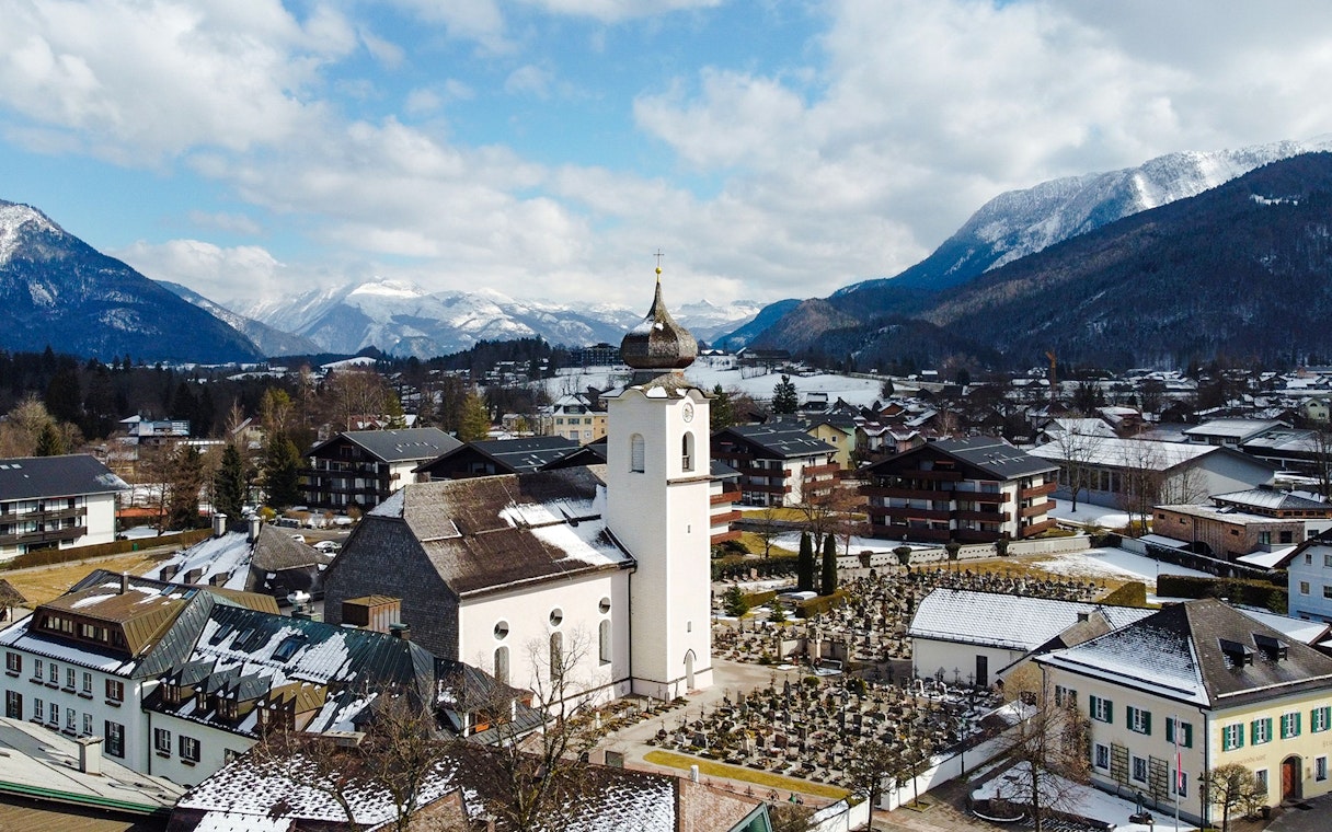 St. Wolfgang chapel in winter, surrounded by snow-covered buildings and mountains, Austria.