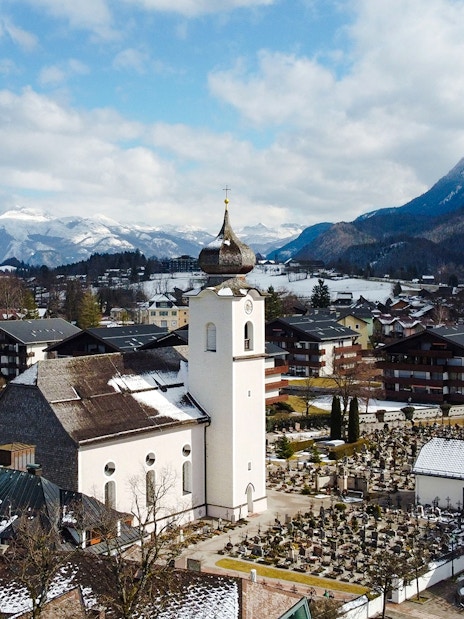 St. Wolfgang chapel in winter, surrounded by snow-covered buildings and mountains, Austria.