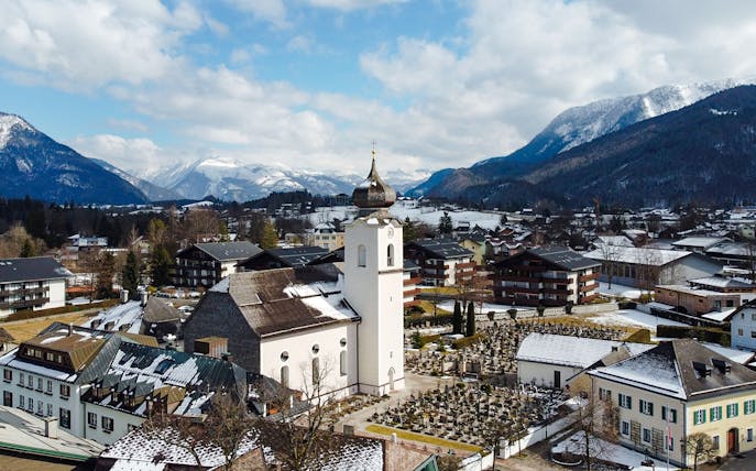 St. Wolfgang chapel in winter, surrounded by snow-covered buildings and mountains, Austria.