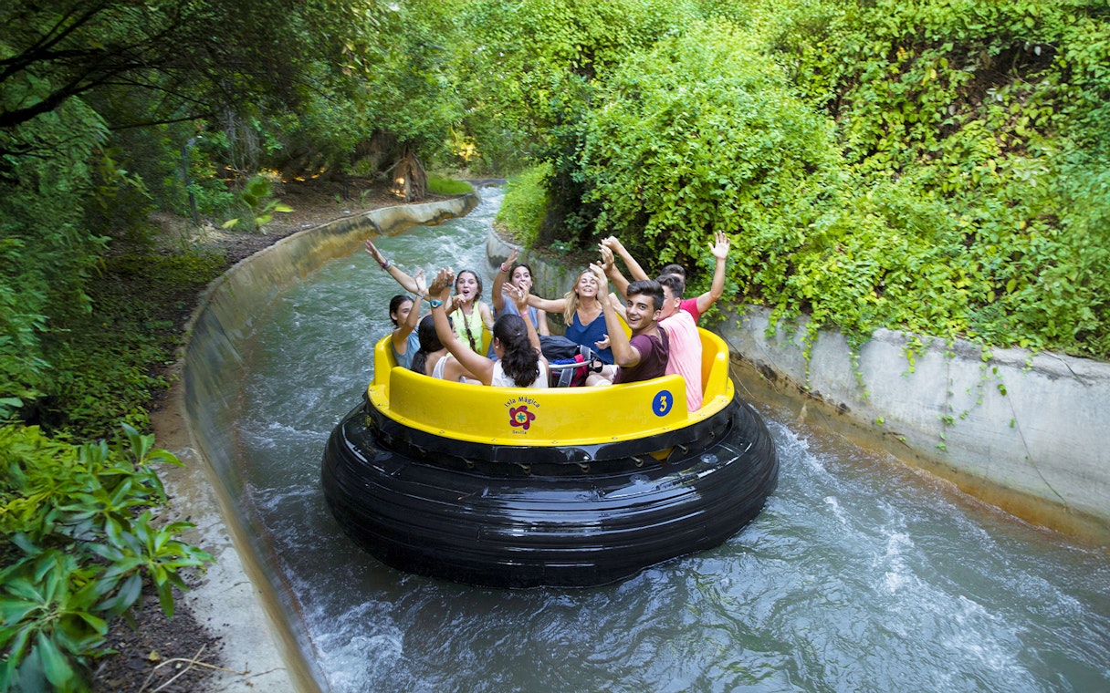 Visitors enjoying a lazy river ride at Isla Mágica, surrounded by lush greenery.