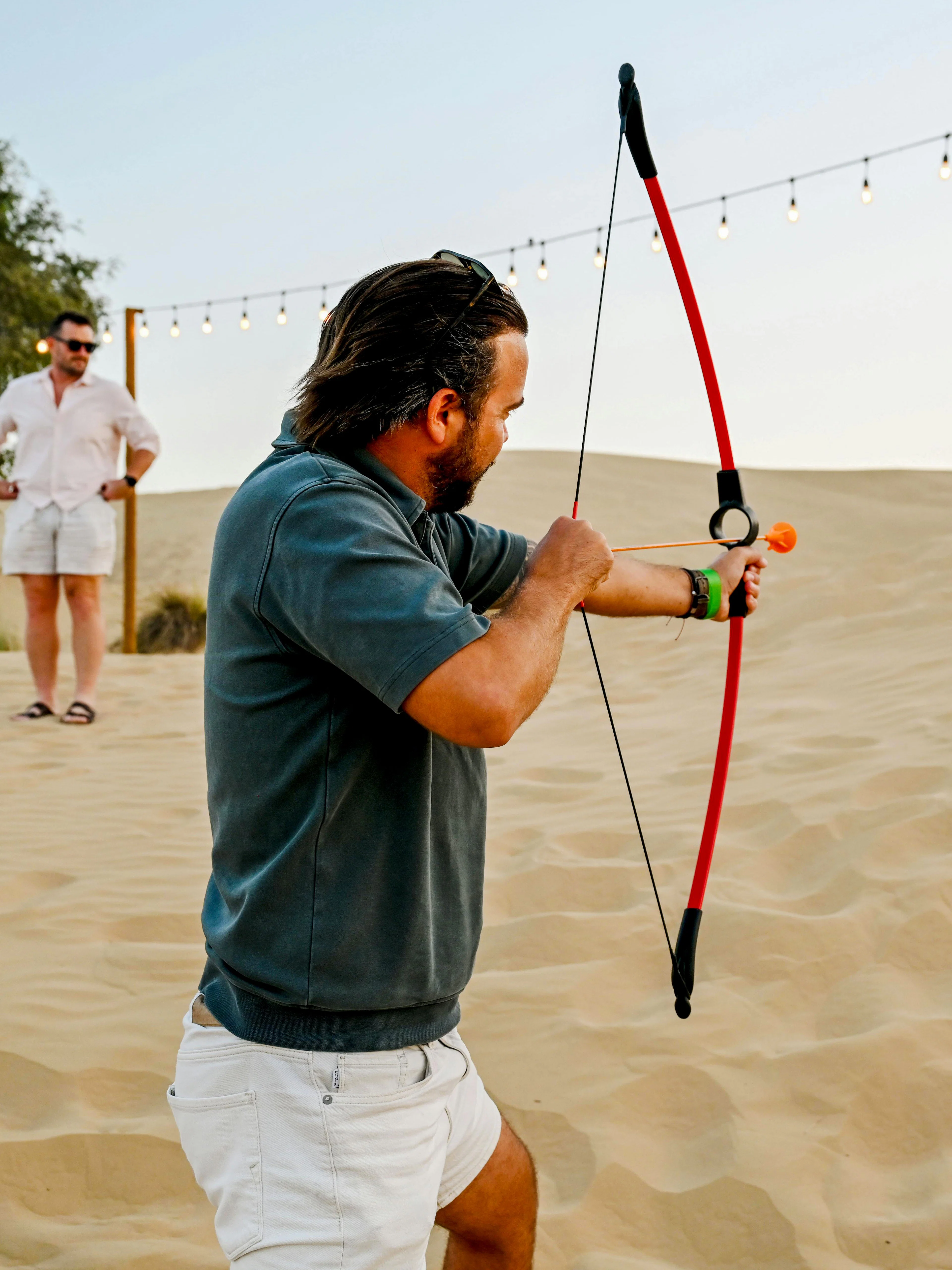 Man practicing archery at Dubai desert safari with target in sand dunes.