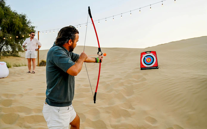 Man practicing archery at Dubai desert safari with target in sand dunes.