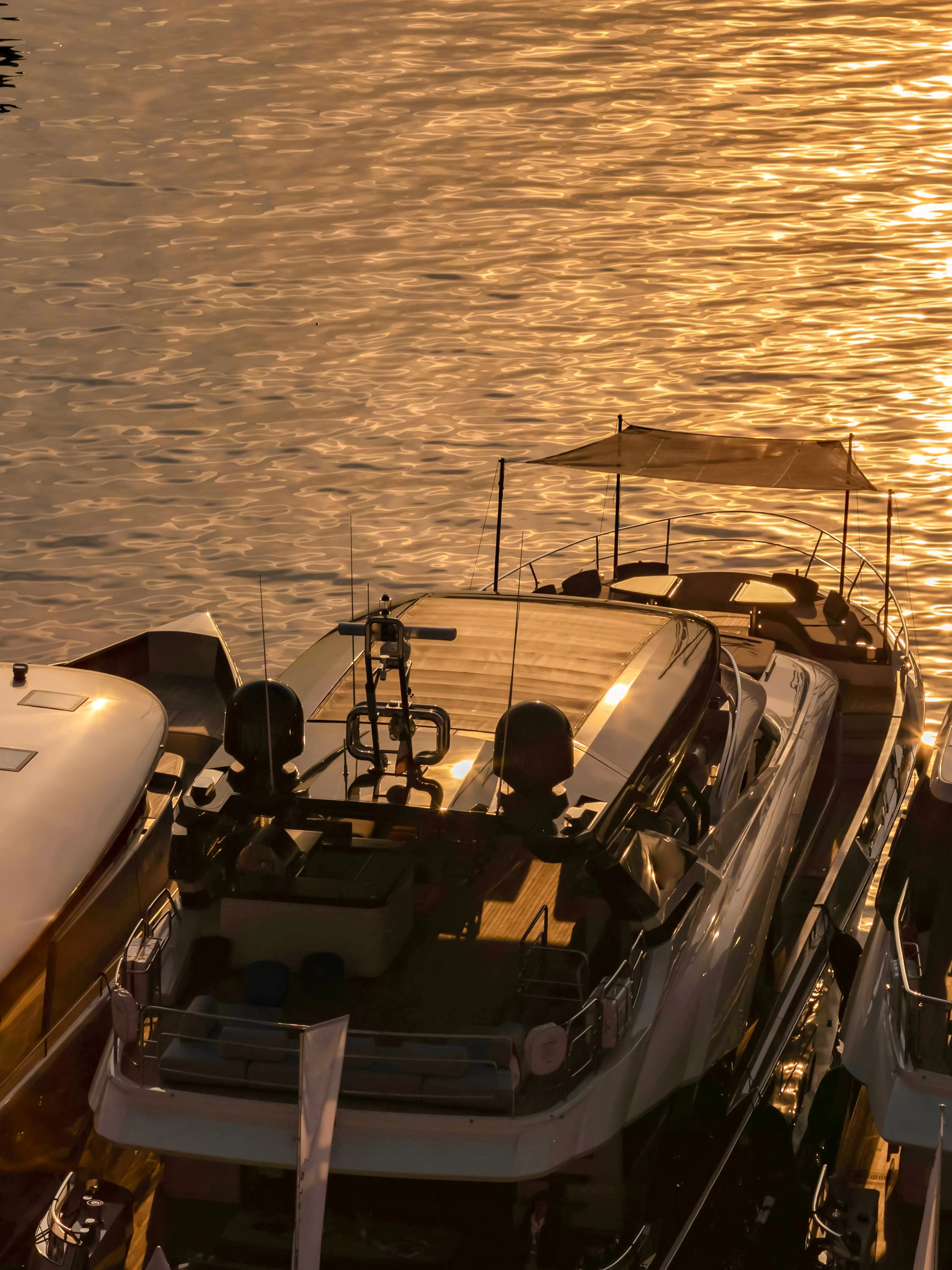 Luxury motor boats moored in Monaco marina at sunrise with sun reflections on water.