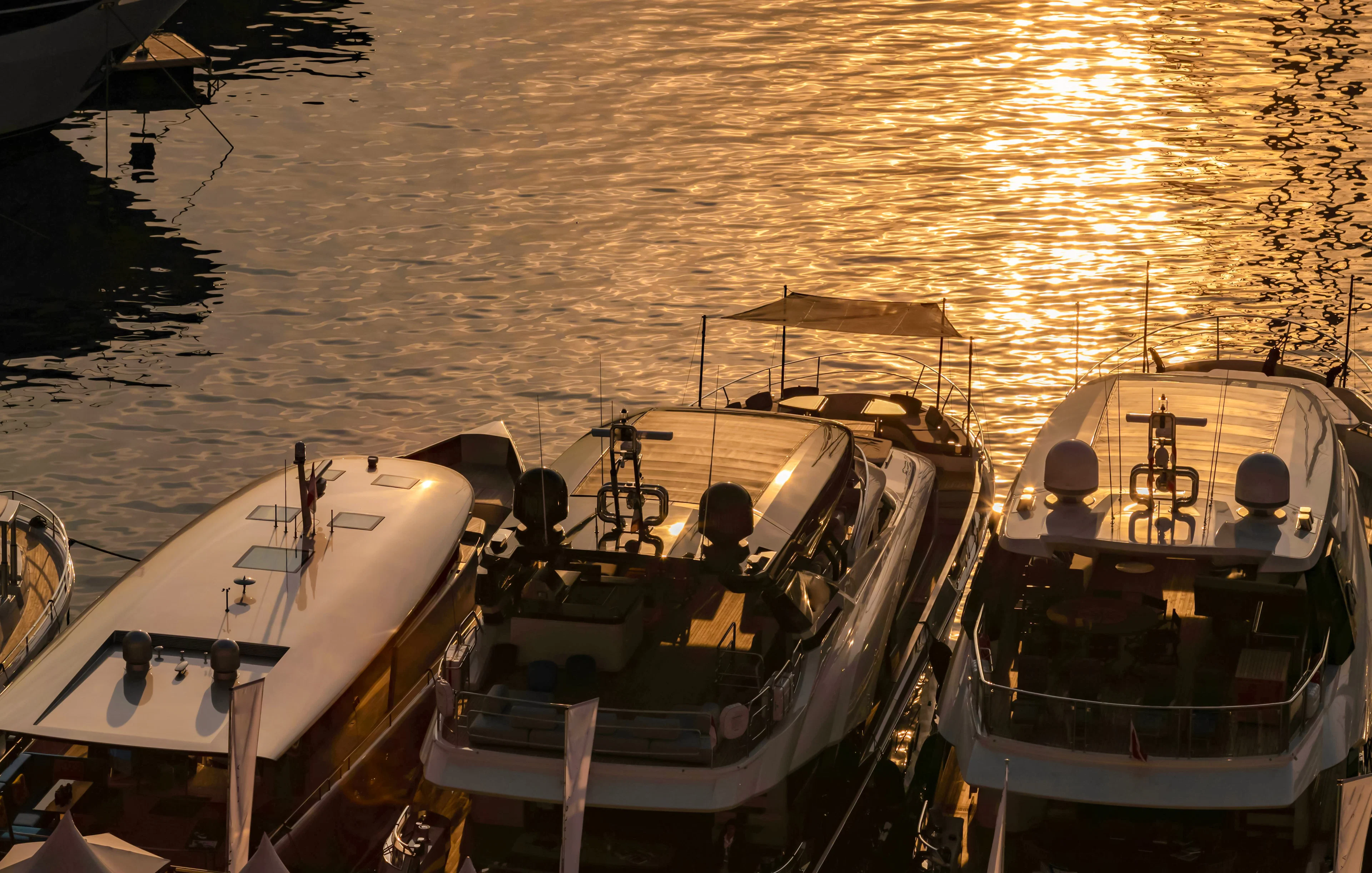 Luxury motor boats moored in Monaco marina at sunrise with sun reflections on water.