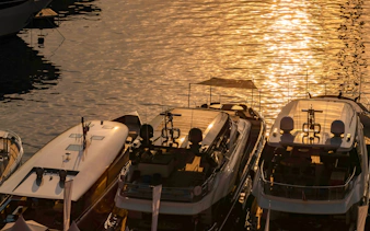 Luxury motor boats moored in Monaco marina at sunrise with sun reflections on water.