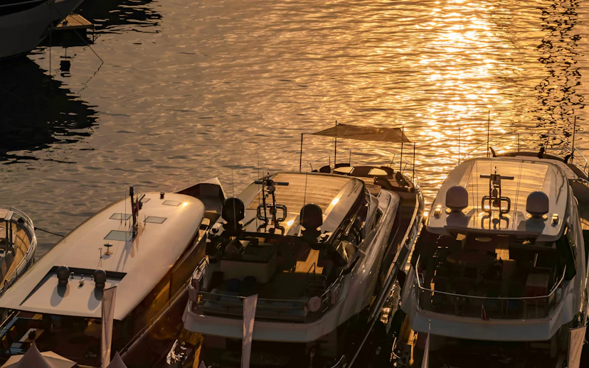 Luxury motor boats moored in Monaco marina at sunrise with sun reflections on water.