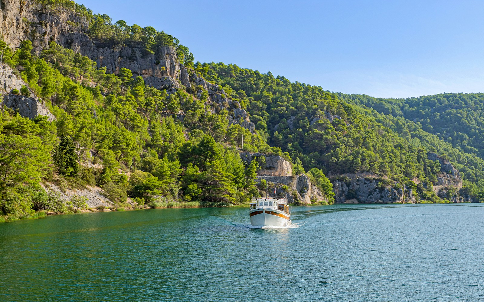 Scenic boat tour on Krka River with lush greenery and cascading waterfalls in Krka National Park, Croatia.