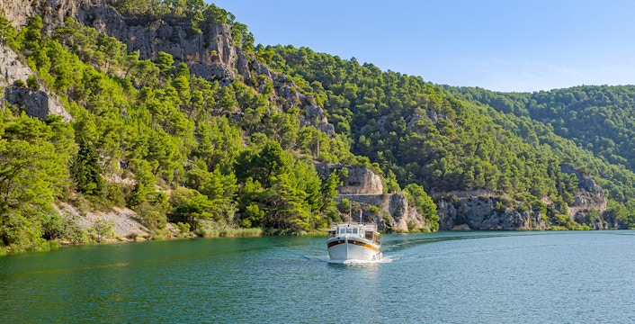 Boat cruising through Krka National Park with lush green cliffs.