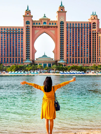 Female tourist in Dubai posing in front of Atlantis Hotel with arms outstretched.