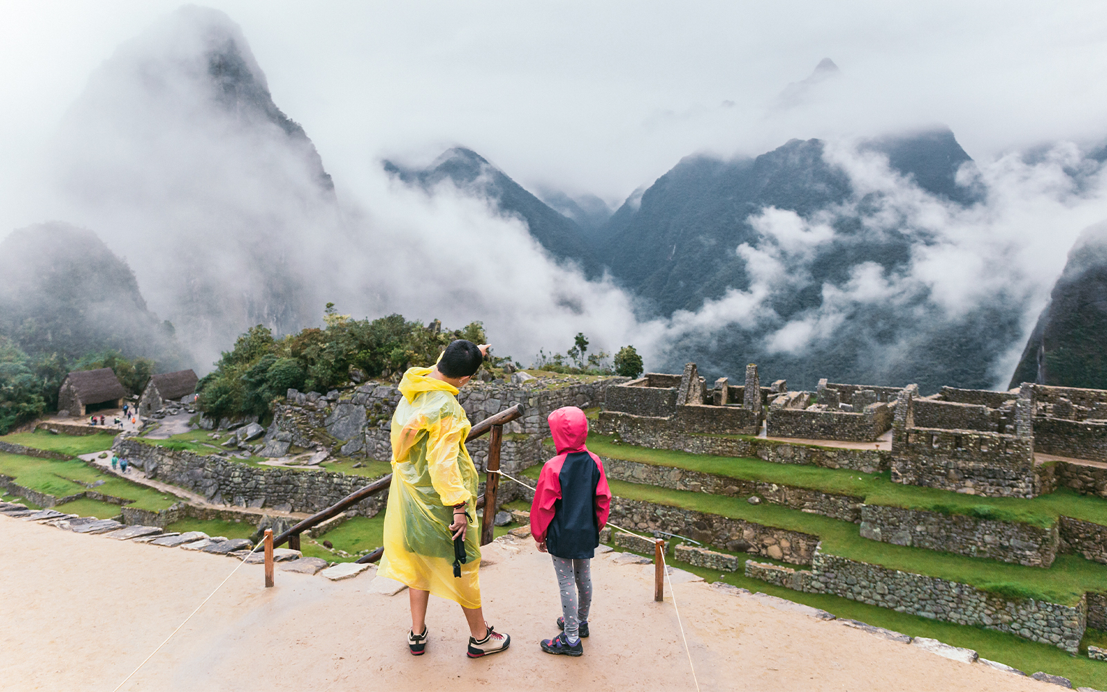 Mother and child in rain jackets exploring Machu Picchu ruins, Peru.