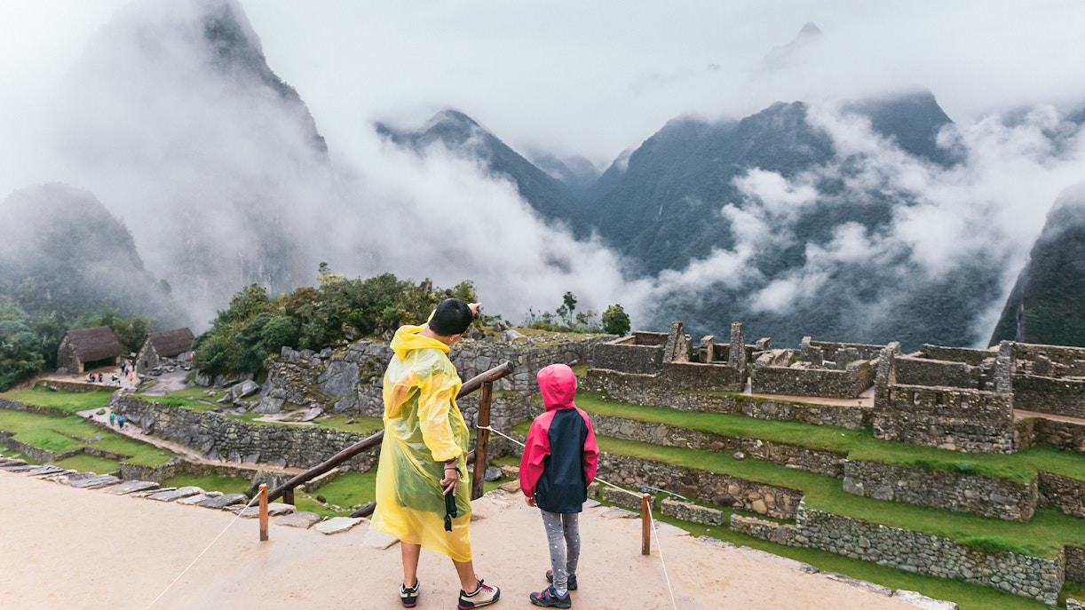 Mother and child in rain jackets overlooking Machu Picchu ruins.