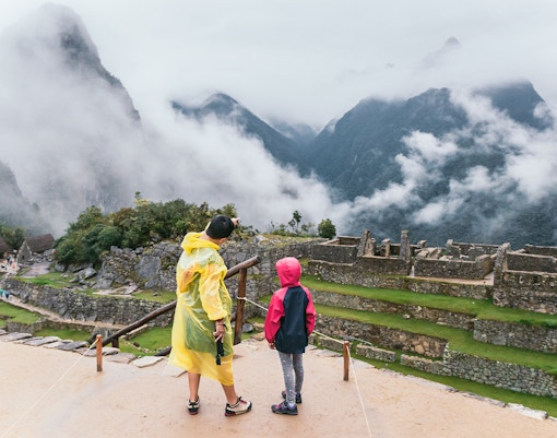 Mother and child in rain jackets overlooking Machu Picchu ruins.