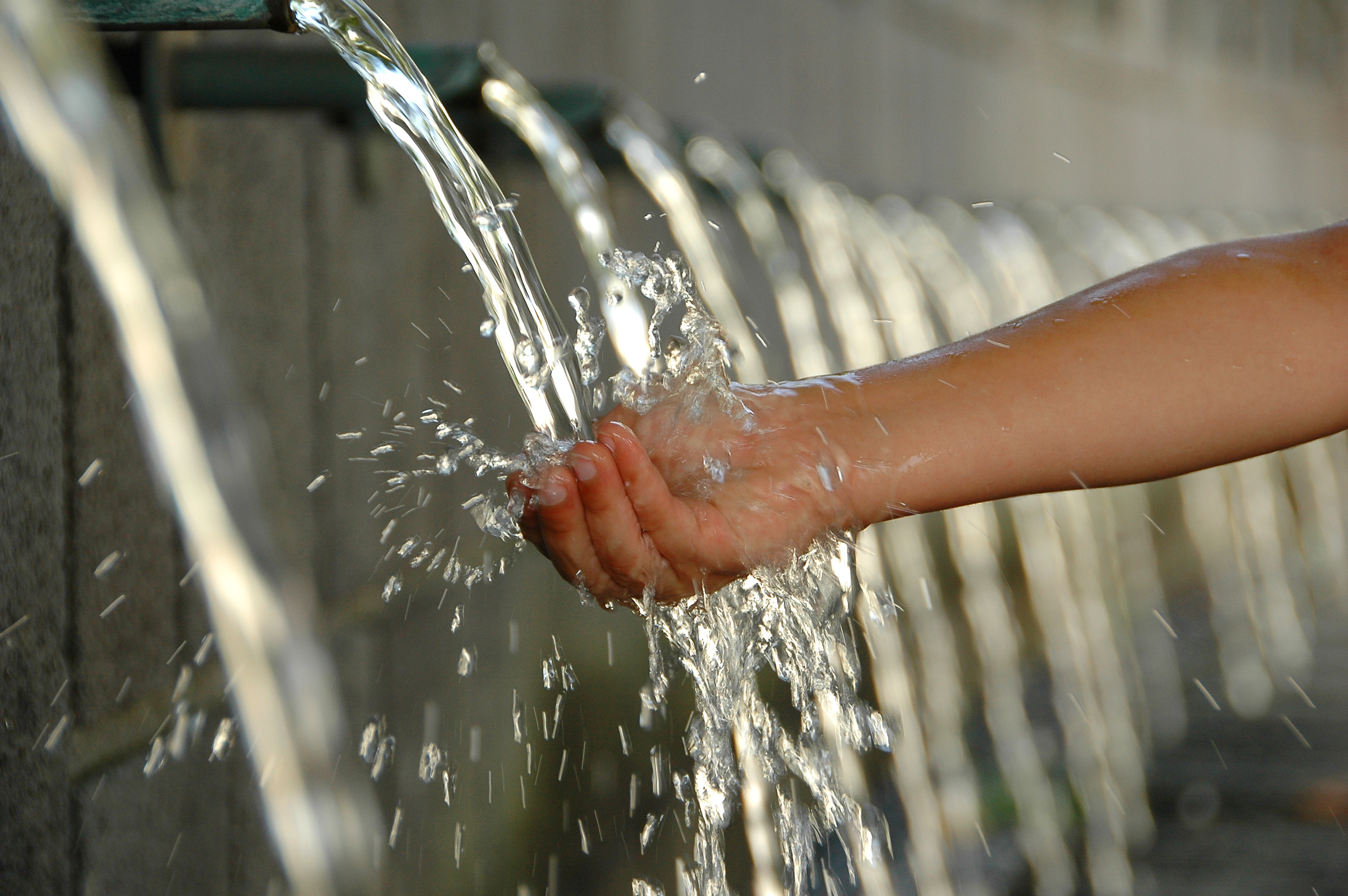 Hand catching water from waterworks building spout.