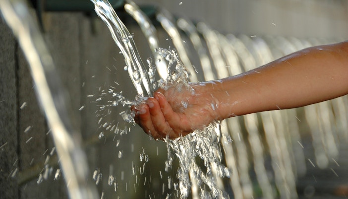 Hand catching water from waterworks building spout.