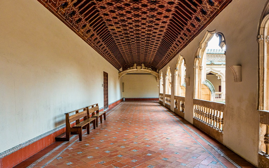 Monastery of San Juan de los Reyes corridor with ornate ceiling and arched windows, Toledo, Spain.
