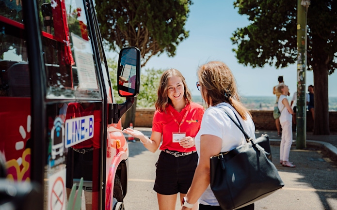 Tour guide assisting a visitor near a City Sightseeing Verona hop-on hop-off bus.