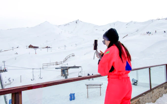 Person in bright outfit photographing snowy Valle Nevado ski slopes, Santiago.