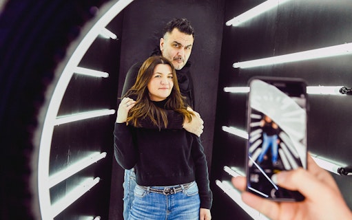 Couple posing in Thessaloniki Selfie Museum with neon lights and phone camera.