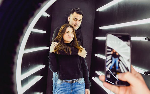 Couple posing in Thessaloniki Selfie Museum with neon lights and phone camera.