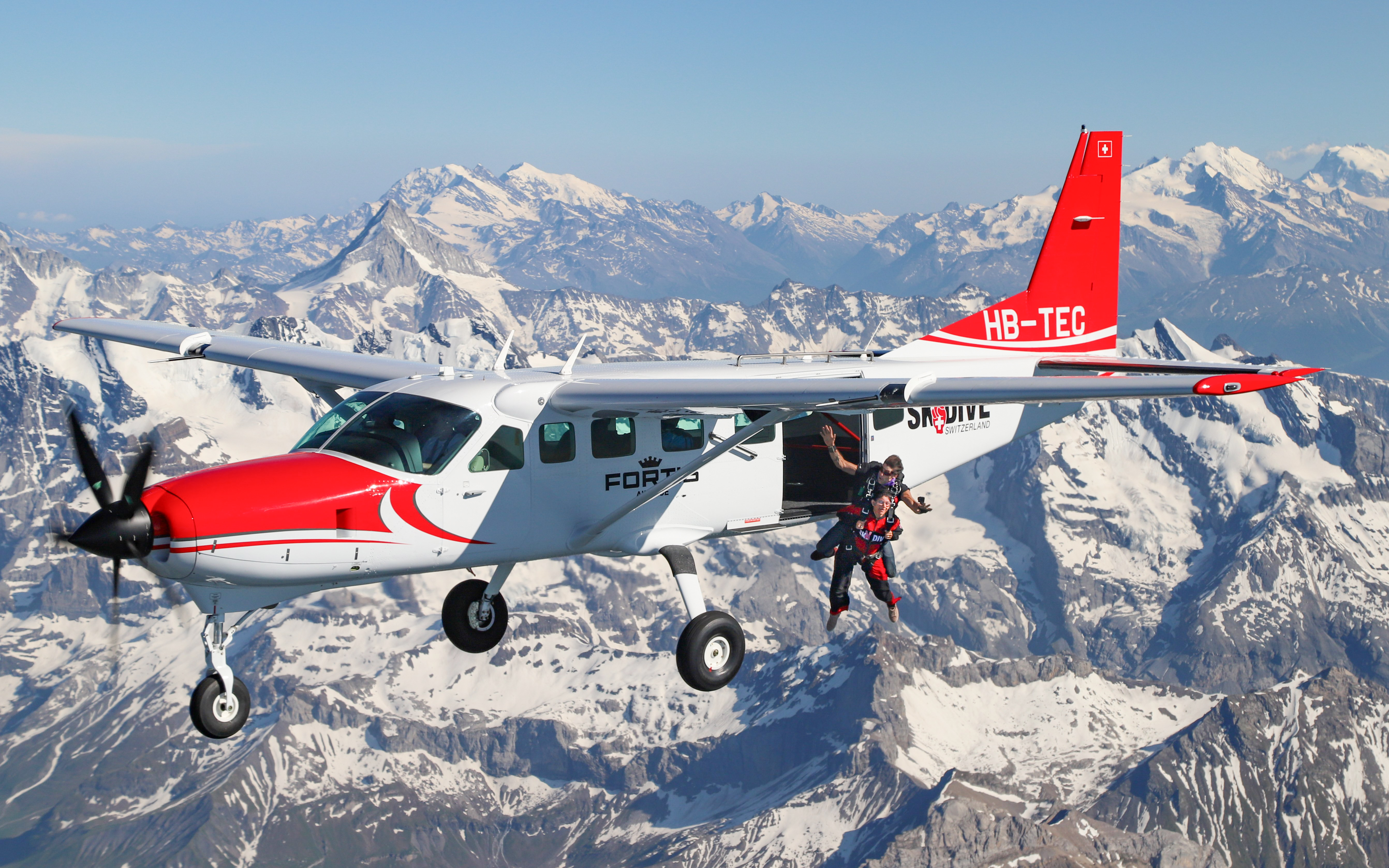 Skydivers jumping from a plane over the Swiss Alps.