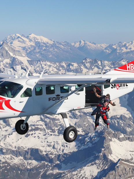 Skydivers jumping from a plane over the Swiss Alps.