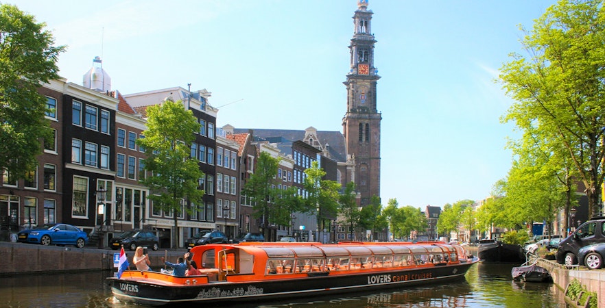 Canal cruise boat on Amsterdam canal with Westerkerk tower in the background.