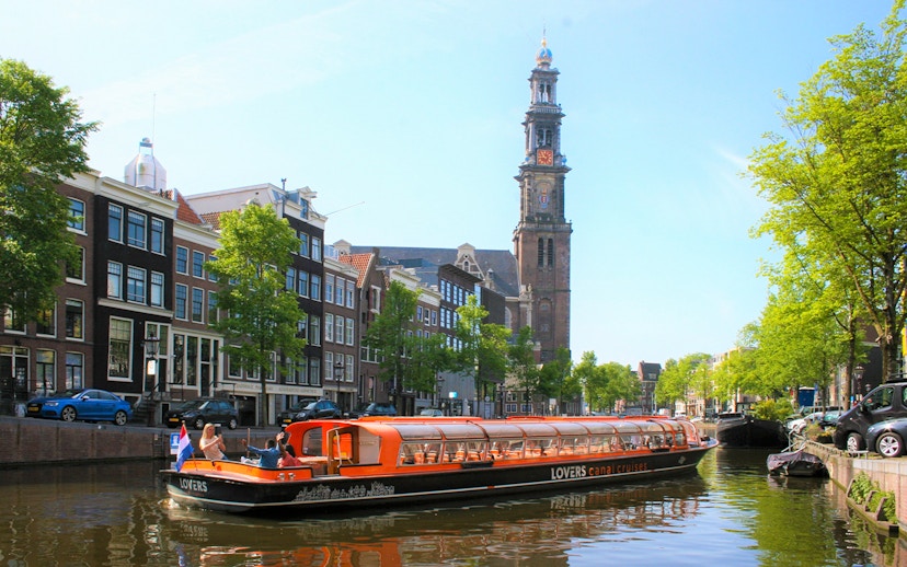 Canal cruise boat on Amsterdam canal with Westerkerk tower in the background.