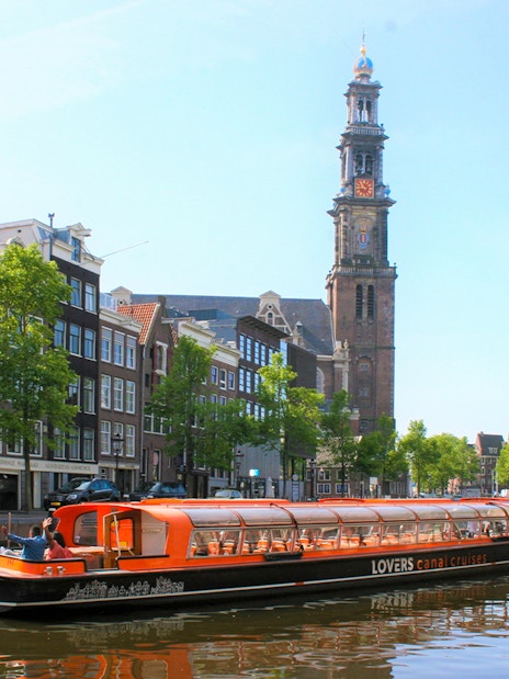 Canal cruise boat on Amsterdam canal with Westerkerk tower in the background.