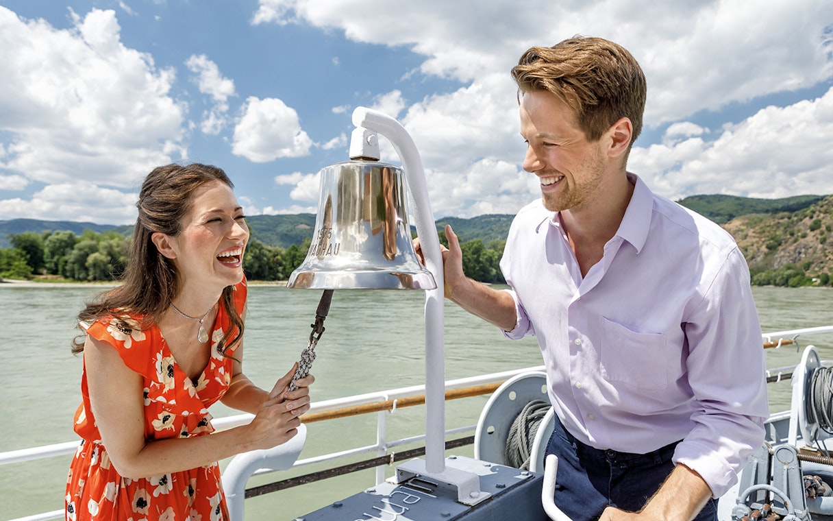 Couple ringing a bell on a boat during Wachau day trip with Melk in the background.