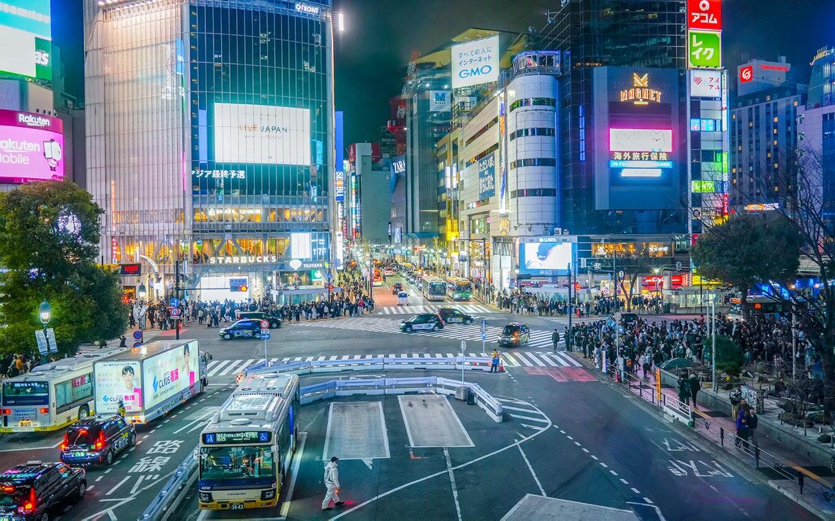 Shibuya Crossing view from Shibuya Sky Deck, Tokyo, with bustling crowds and illuminated buildings.