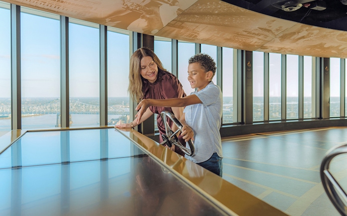 Visitors using viewfinder at Vue Orleans Observation Deck overlooking New Orleans city.
