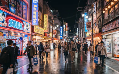 Shoppers explore Osaka's Den Den Town at night, featuring anime and retro game stores.