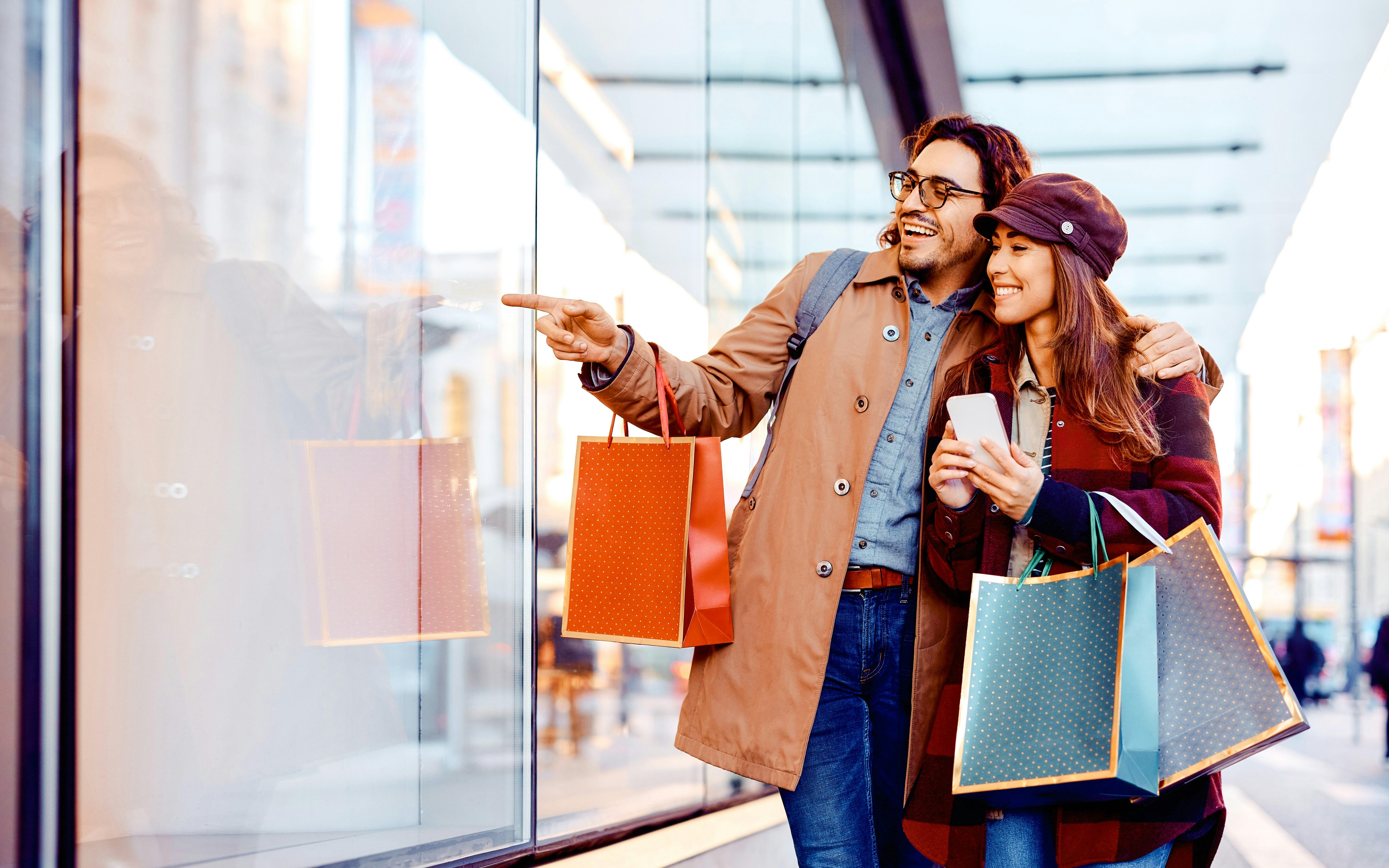 Couple shopping at La Vallee Village, Paris, holding bags and pointing at a store window.