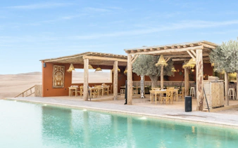 Outdoor dining area at Les Terrasses d'Agafay camp with pool and desert view.