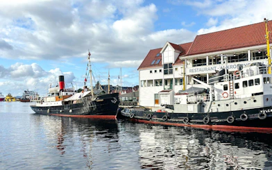 Historic ships docked at Bergen Pier, Norway, with waterfront buildings in the background.